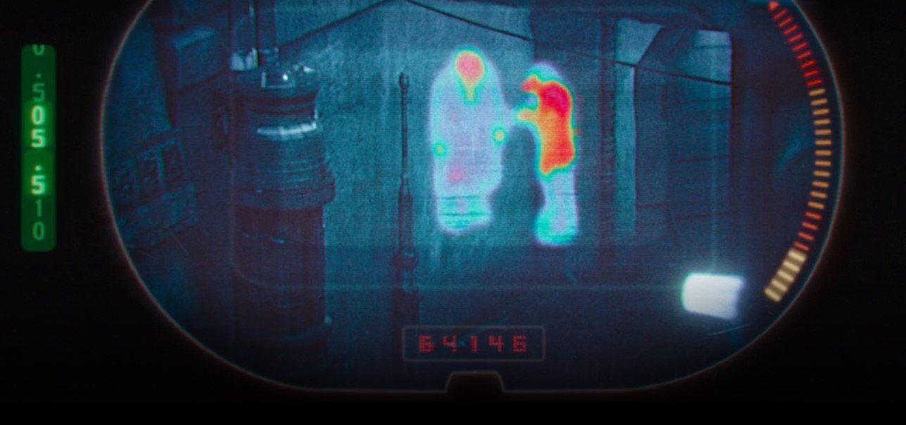 View through the heads up display showing two humanoid figures stood together in thermal imaging; on the left we see a rotating dial display with the numbers "0 . 505 . 510" and at the bottom "64146"